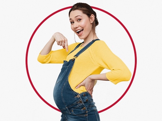 Glad, ung, gravid kvinne iført gul genser, som peker på magen sin