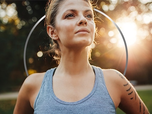 Aktiv ung kvinne i singlet, som står i en kraftfull positur med solen i bakgrunnen