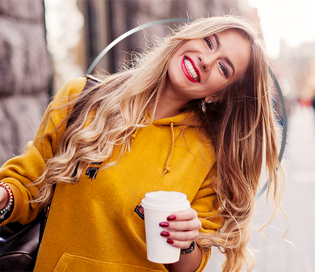 Glad ung kvinne med gul hettegenser som holder en kaffekopp i papp