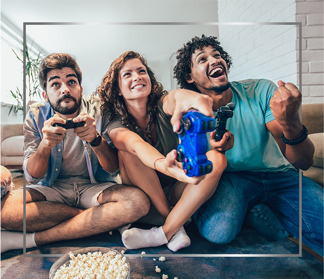 Gruppe av unge smilende mennesker som sitter på gulvet og spiller videospill, glade etter Canesten soppinfeksjonsbehandling